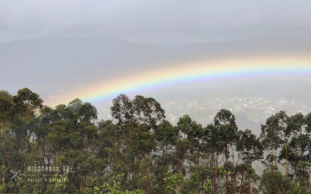 arco iris sobre un valle con montañas, árboles y casas